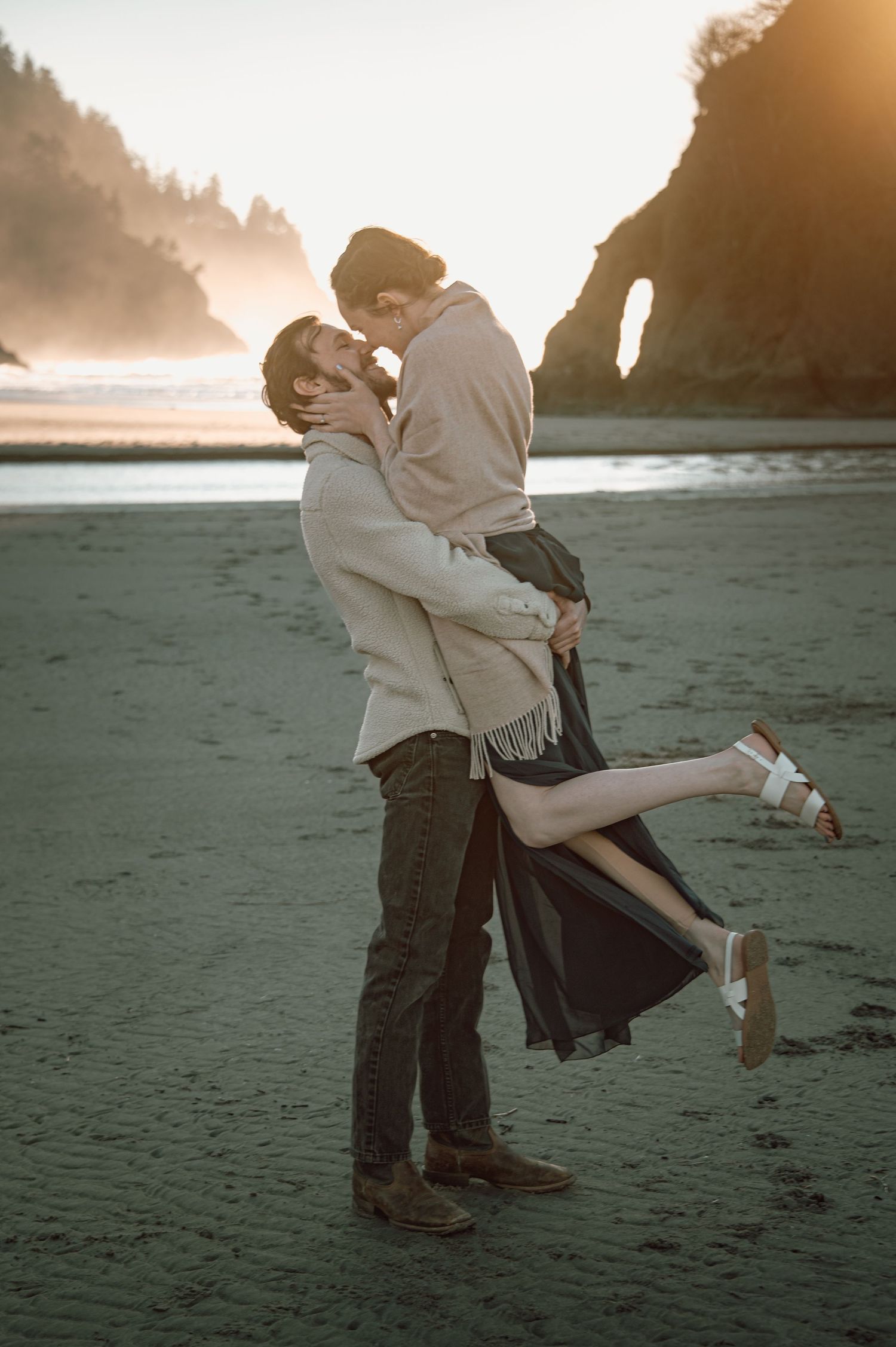 Couple sharing a romantic kiss on a misty beach at sunset, man lifting woman in a tender embrace.  Couple mini photo shoot.