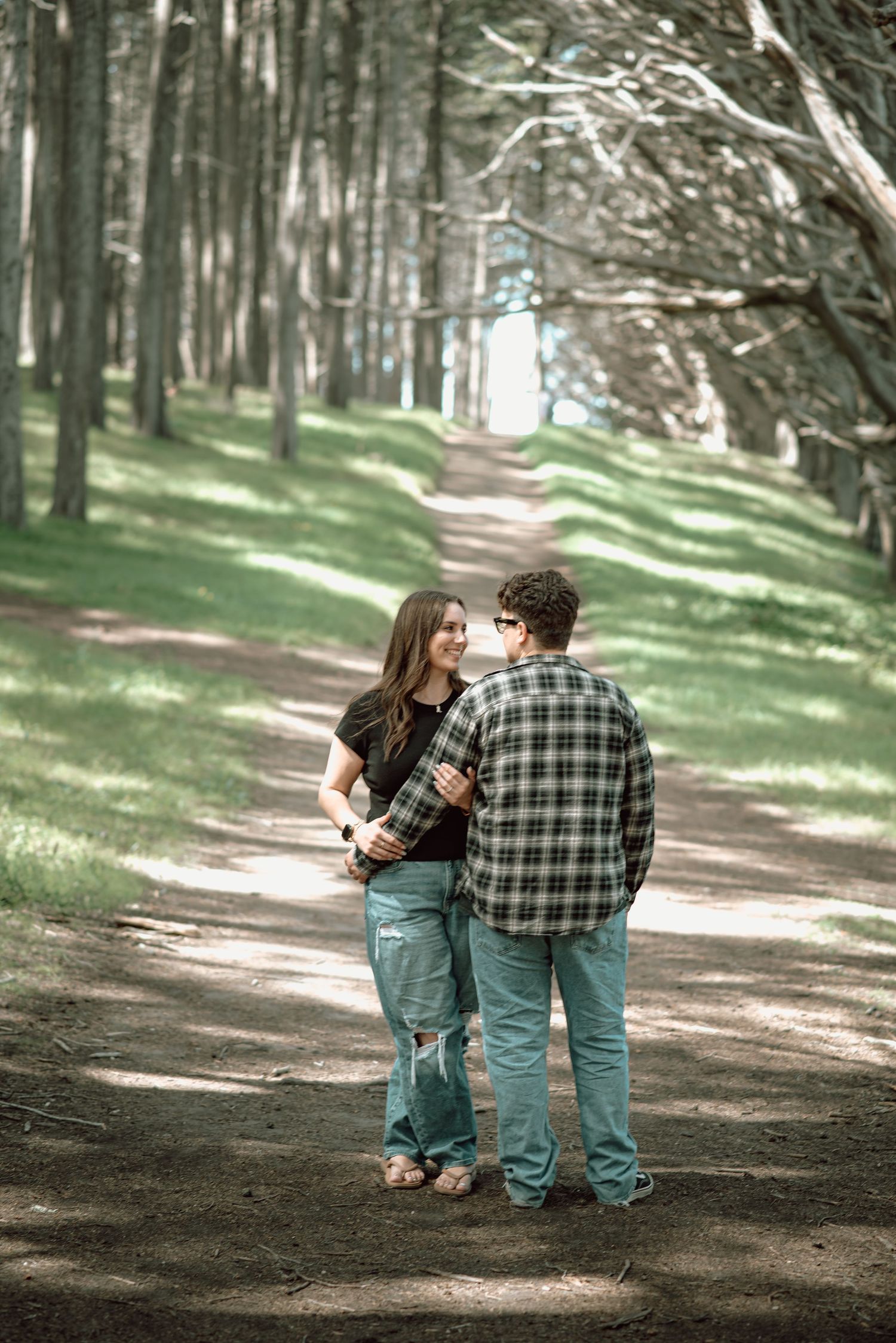 Couple shares a tender moment while walking along a tree-lined forest path.