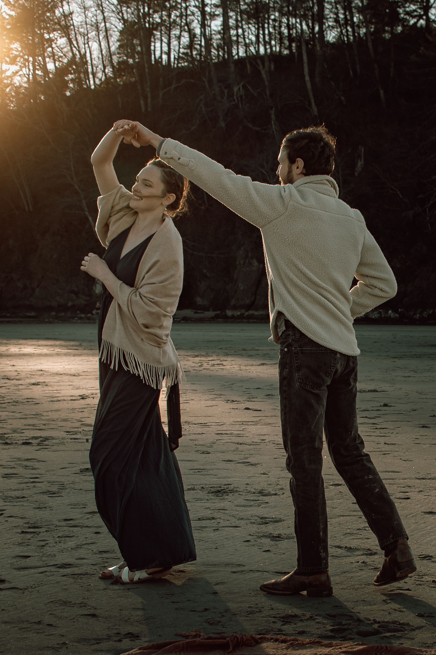 Couple dancing on a beach at sunset, man spinning woman in a fringed shawl and black dress.