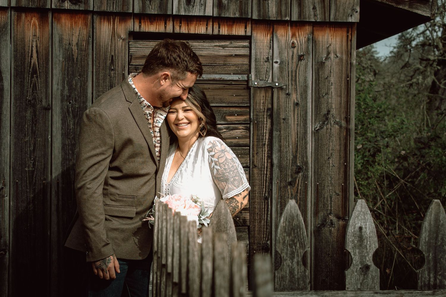 Couple smiling together against rustic wooden barn wall during outdoor wedding photo session.