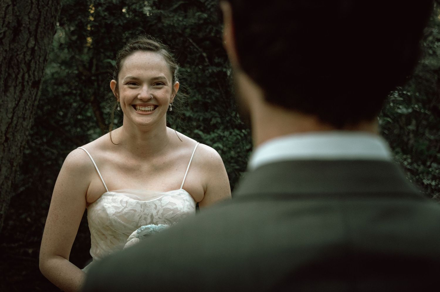 Smiling bride in white strapless gown during outdoor forest wedding ceremony.