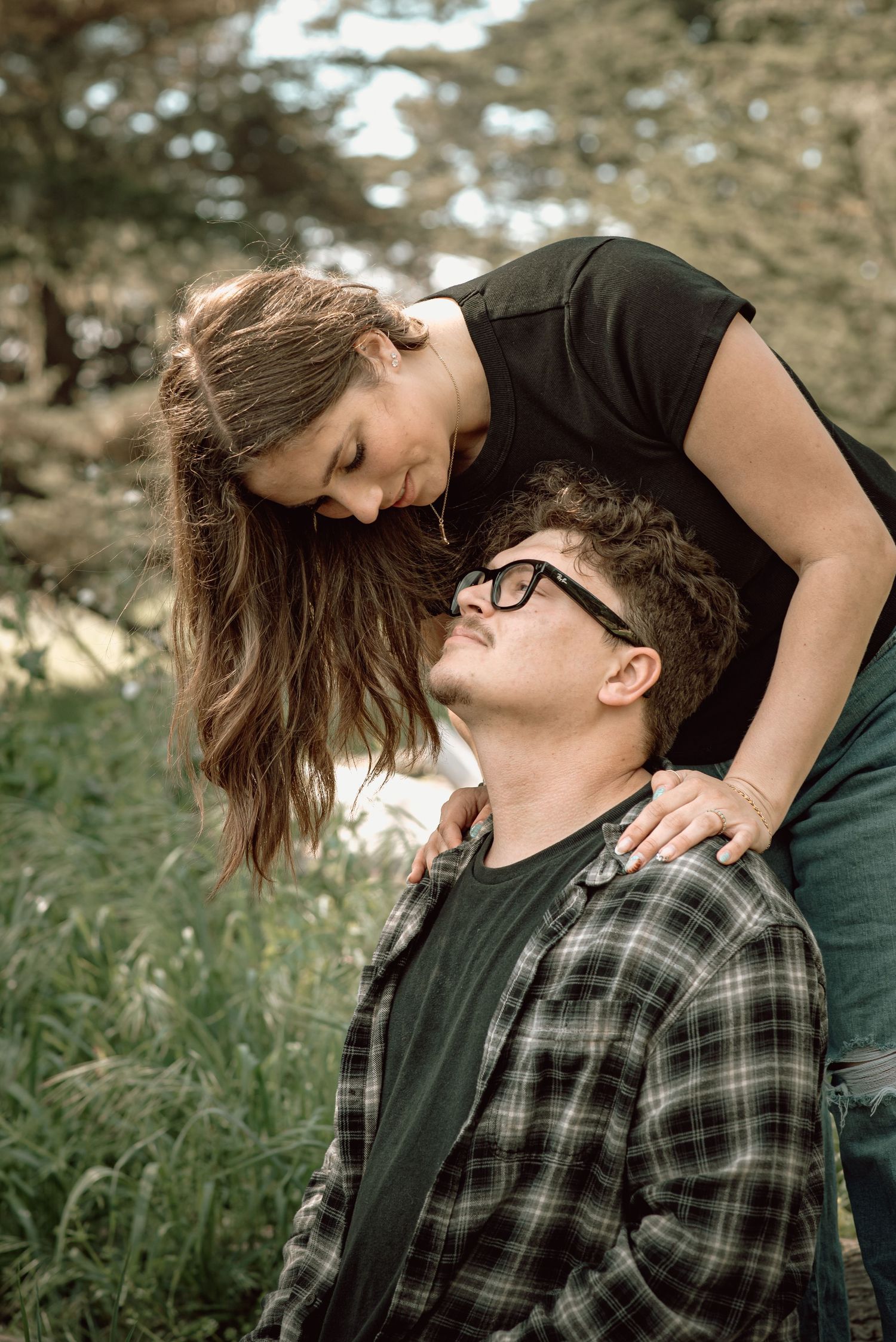 Couple shares an intimate moment outdoors with woman leaning over seated partner.