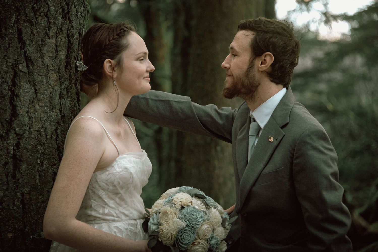 Bride and groom share a tender moment in the forest, with the groom gently touching the bride's face.