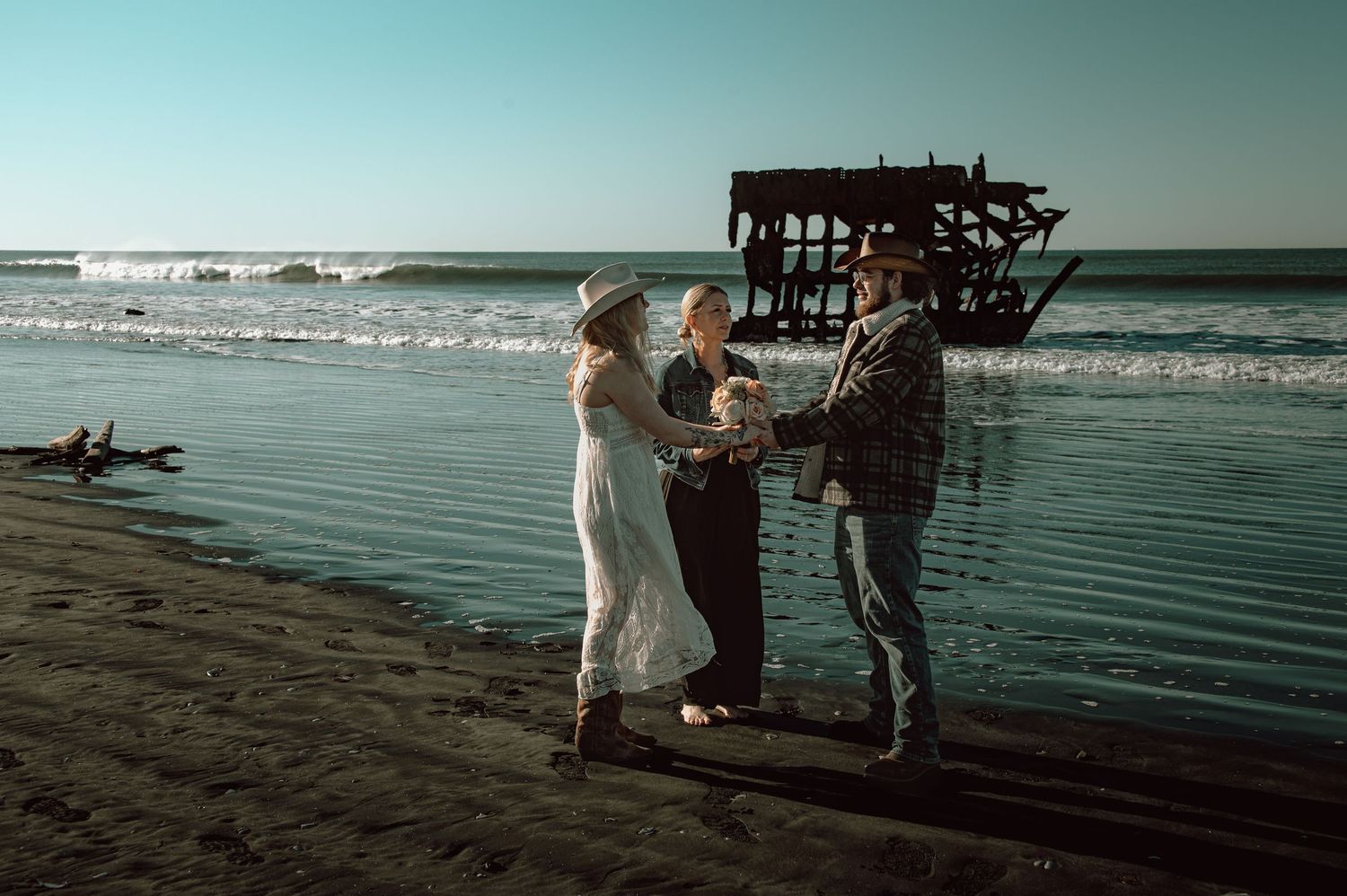 Couple exchanges vows on a scenic beach with a historic shipwreck backdrop during a romantic outdoor elopement ceremony.