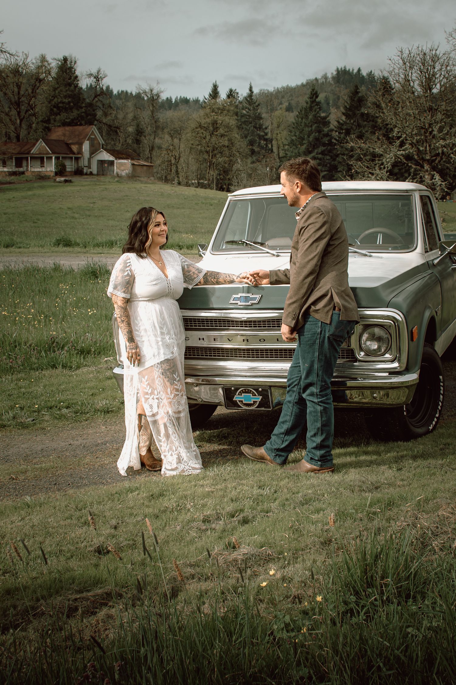 Tattooed bride in white lace dress and groom in olive suit share a moment beside a vintage Chevrolet truck.
