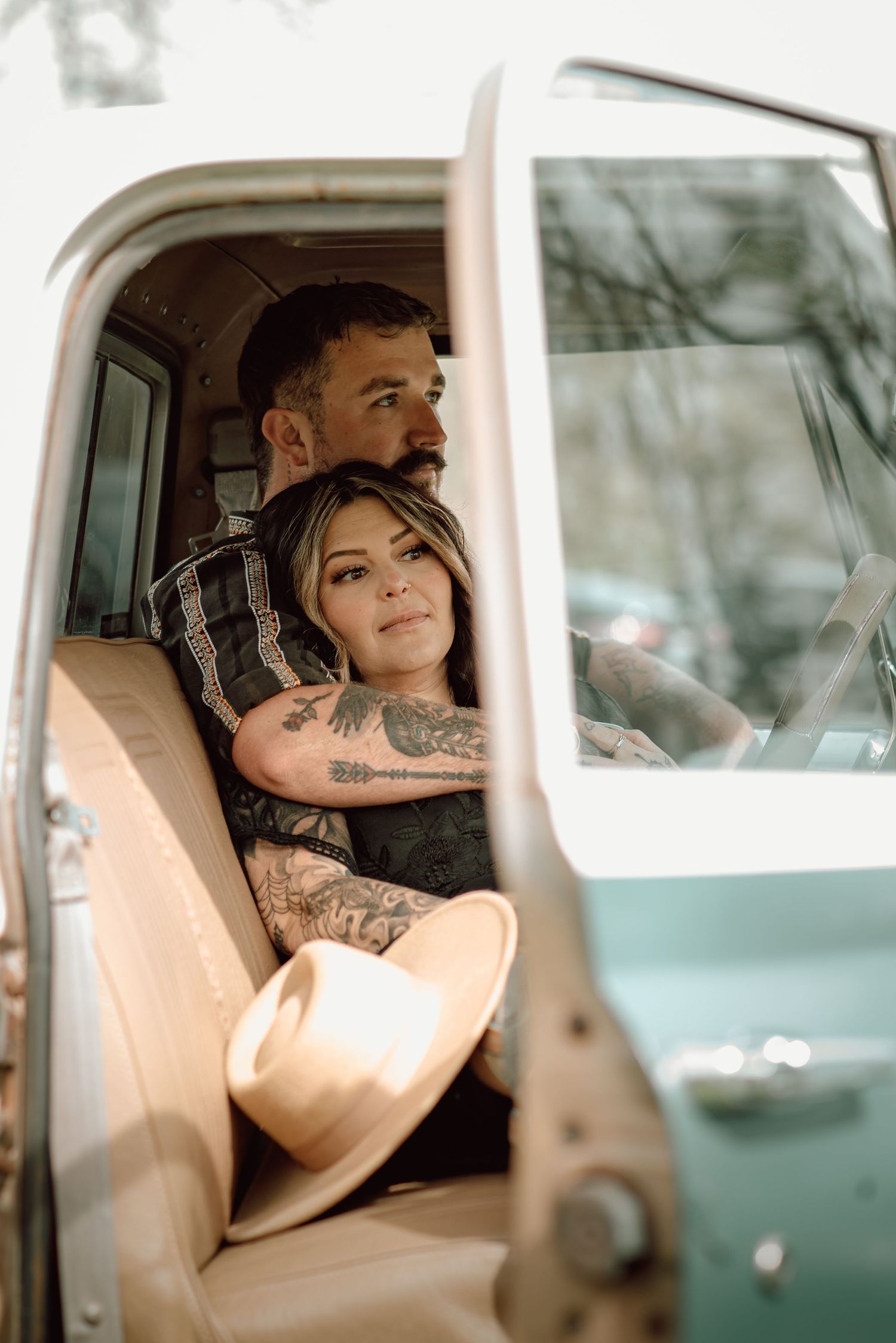 Tattooed couple sitting together inside a vintage teal pickup truck during an engagement session.