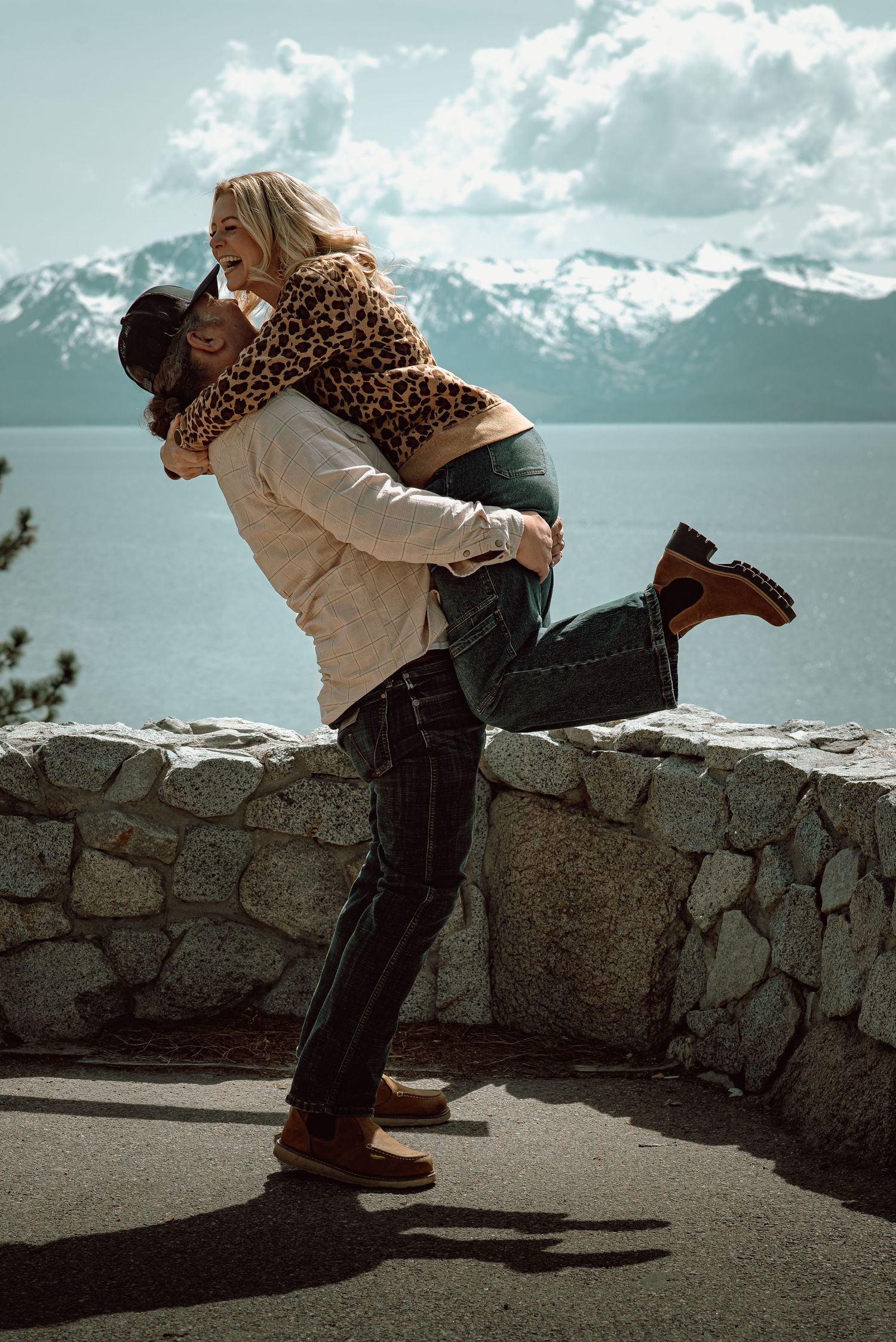 Couple sharing a joyful embrace at Lake Tahoe with snowy mountains in the background.