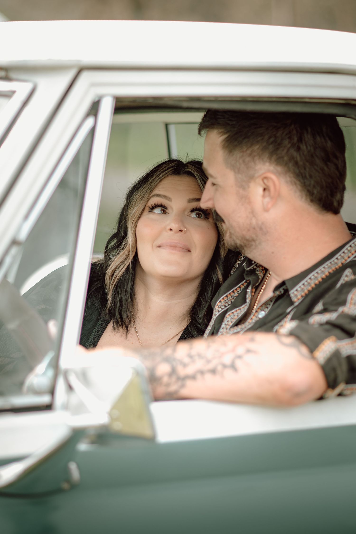 Couple sharing an intimate moment inside a vintage teal truck, the woman gazing up lovingly at the tattooed man.