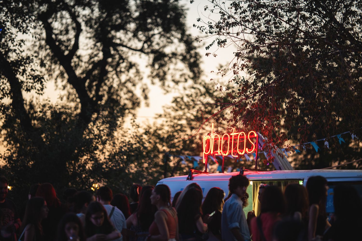Silhouetted crowd gathered at sunset under string lights during an outdoor festival.