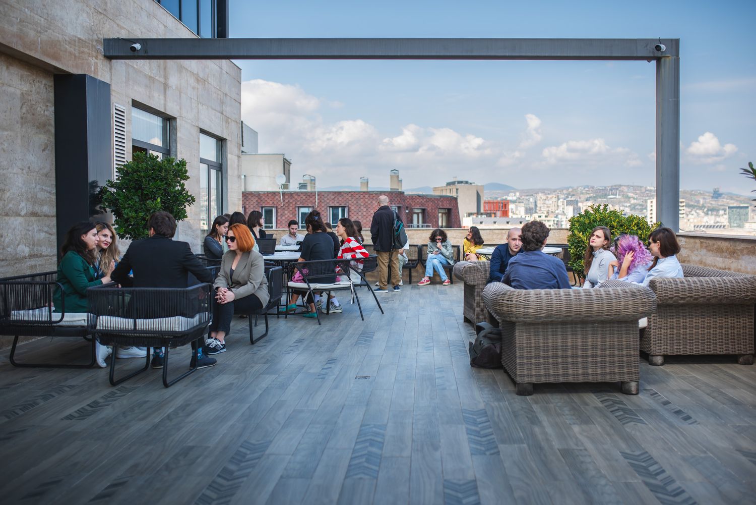 Group of people relaxing and engaging in discussion on a rooftop terrace with a scenic view.