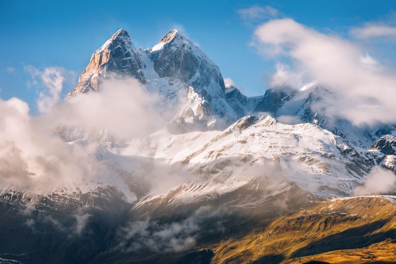 Sharp alpine summit glowing under sunlight, partially veiled by clouds — majestic view of the Caucasus.