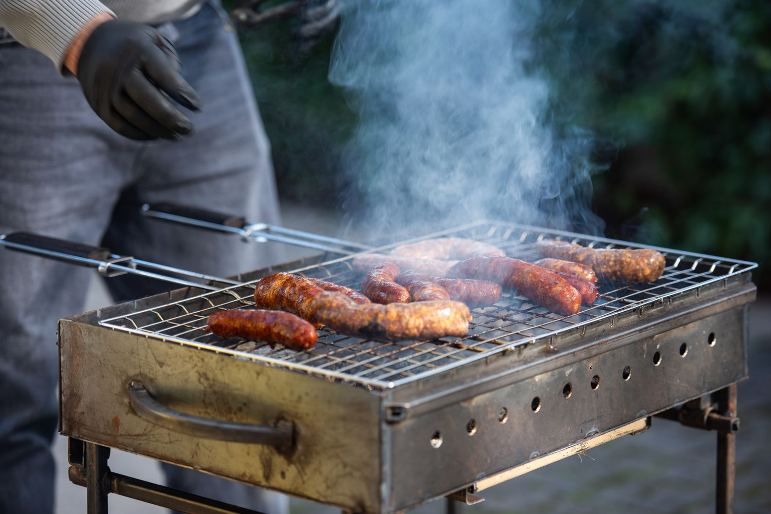 Man grilling meat skewers on a charcoal barbecue outdoors.