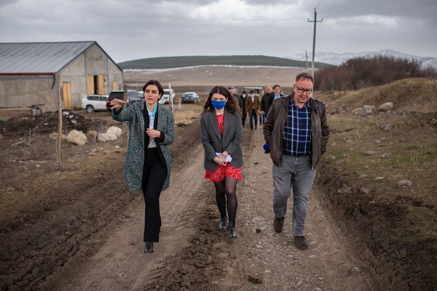 Group of people walking along a muddy rural road during a site visit in the countryside.