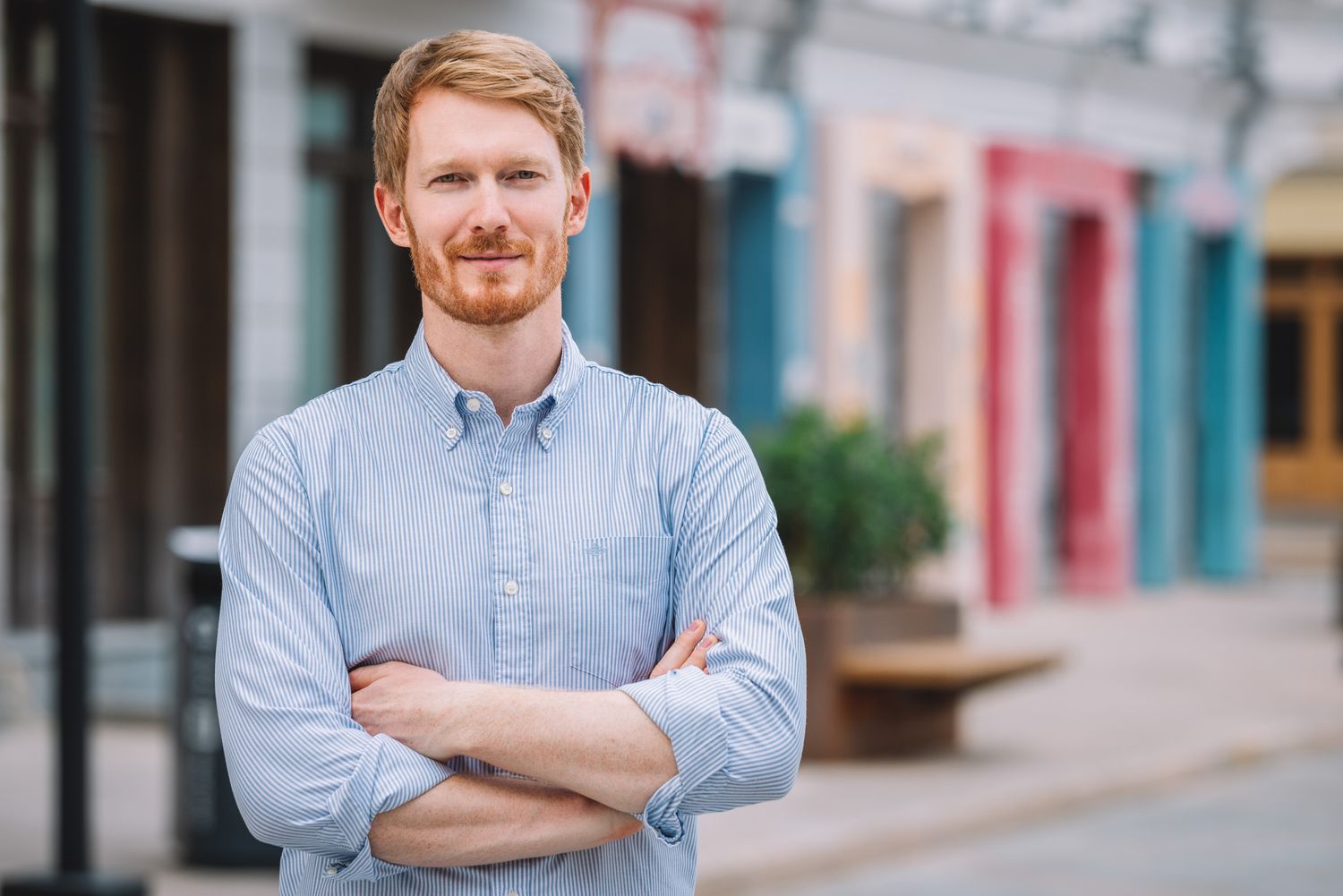 Young professional man posing on a colorful urban street, arms crossed and smiling.