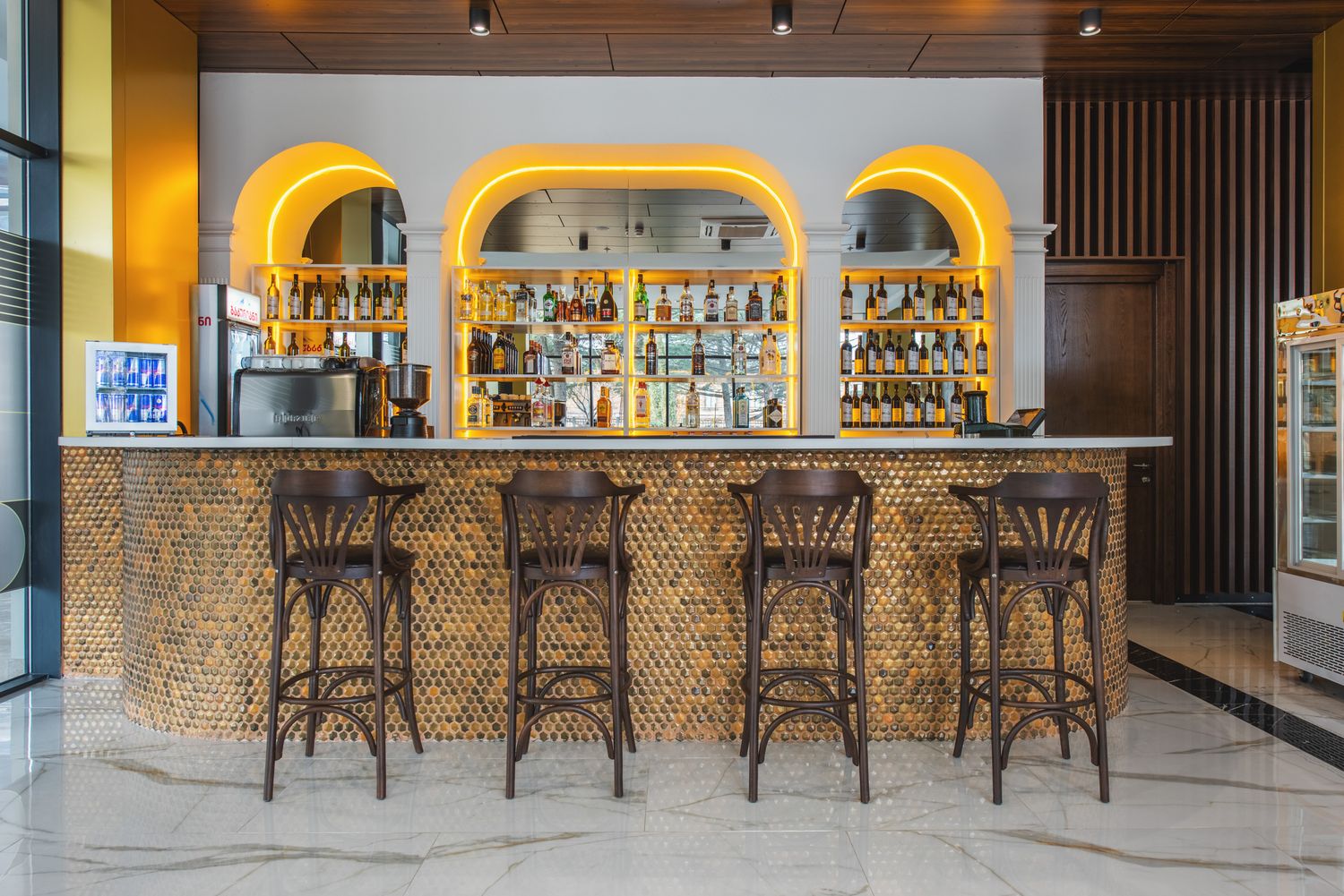 Upscale bar interior with wood and stone finishes, backlit shelving, and elegant pendant lighting.