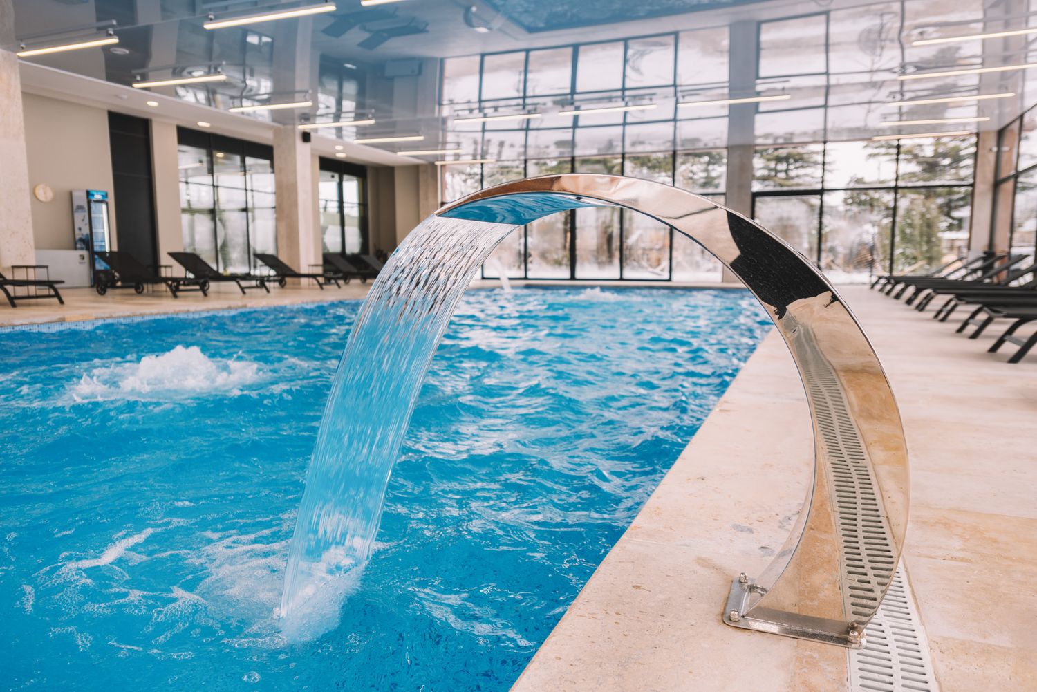 Indoor swimming pool with waterfall feature and glass walls, ideal for spa and wellness facilities.