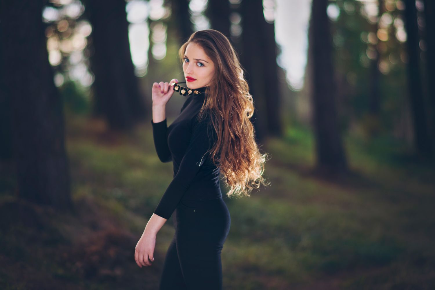 Elegant young woman walking through trees in golden hour light — graceful fashion-style image.