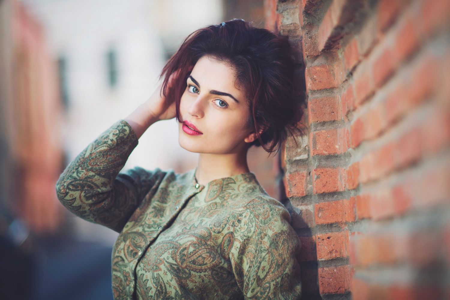 Portrait of a young woman leaning against a brick wall — natural light and confident expression.