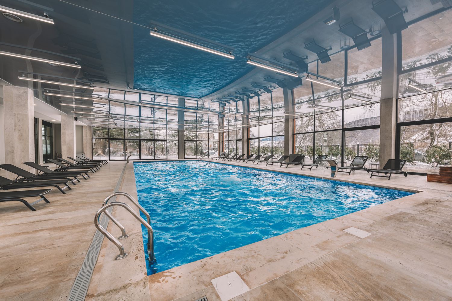 Spacious indoor pool area with wooden ceiling details, lounge chairs, and panoramic windows.
