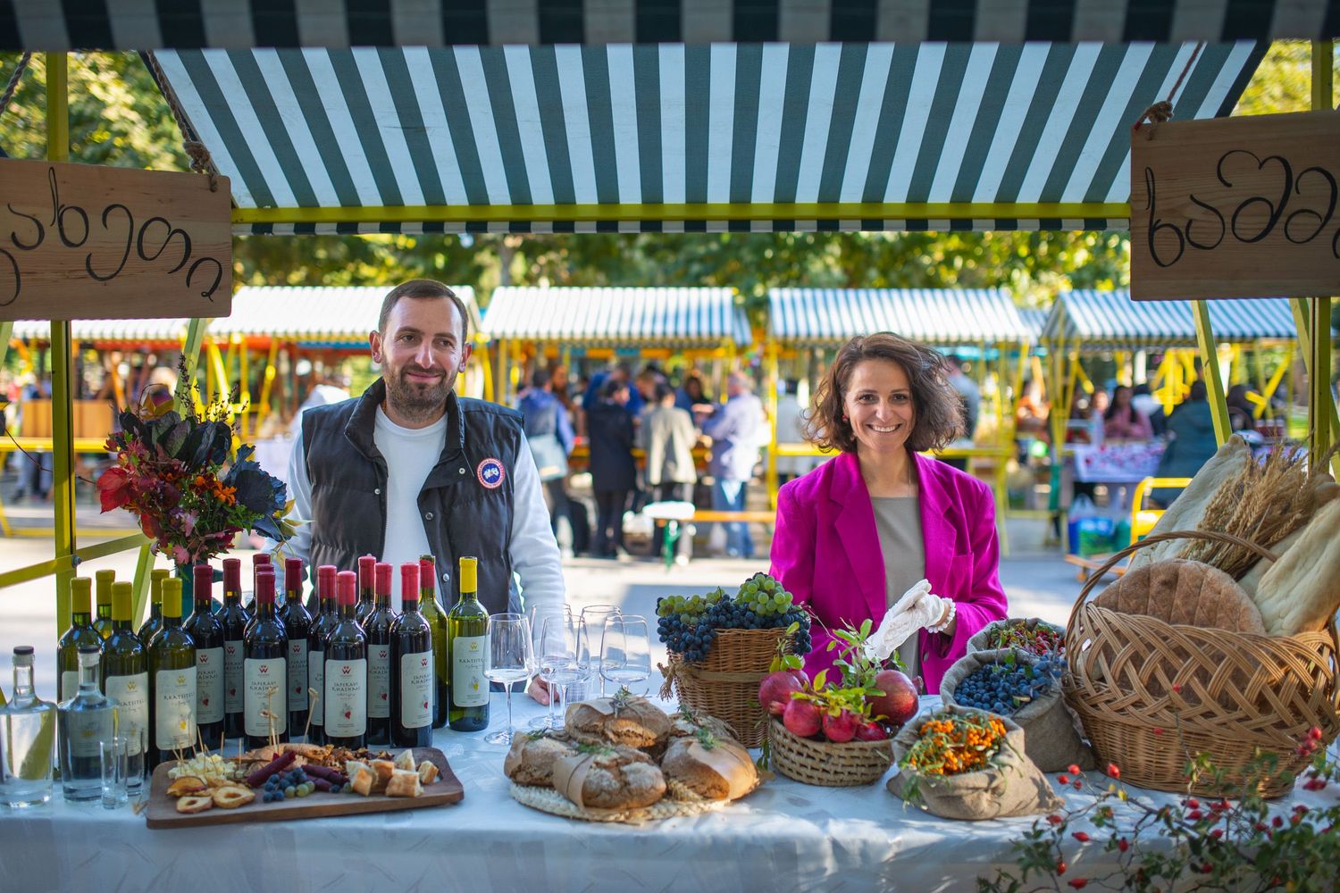 Vendors showcasing local products and wine at an outdoor market under striped tents.
