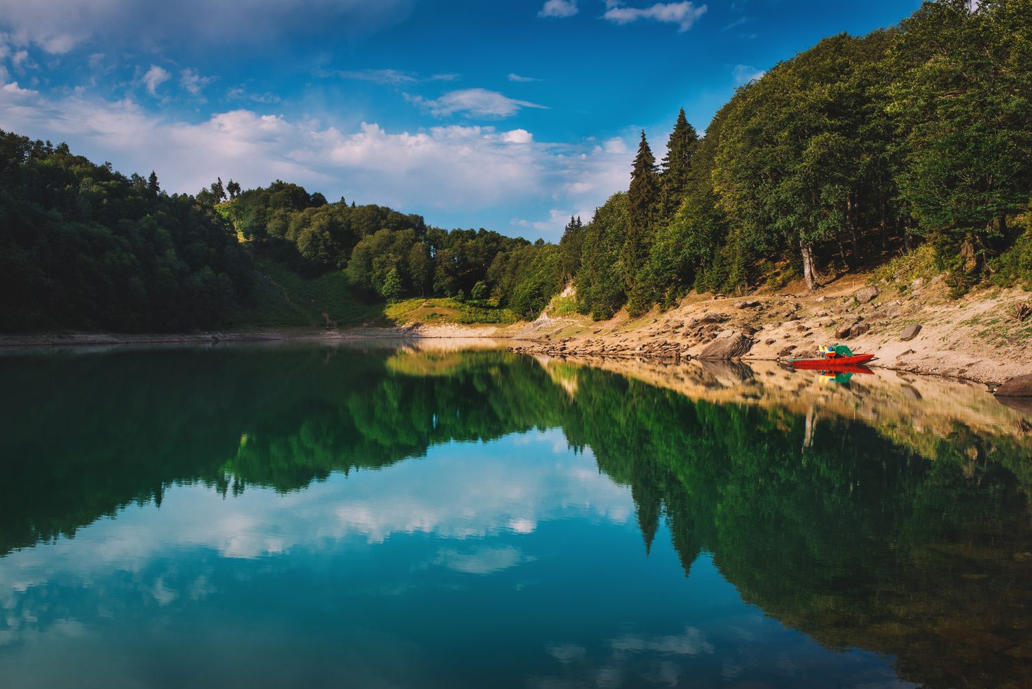 Turquoise mountain lake surrounded by dense evergreen forest under clear summer skies.