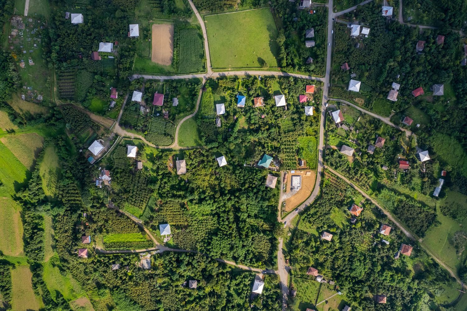 Aerial top-down view of a green countryside village with scattered houses and roads.
