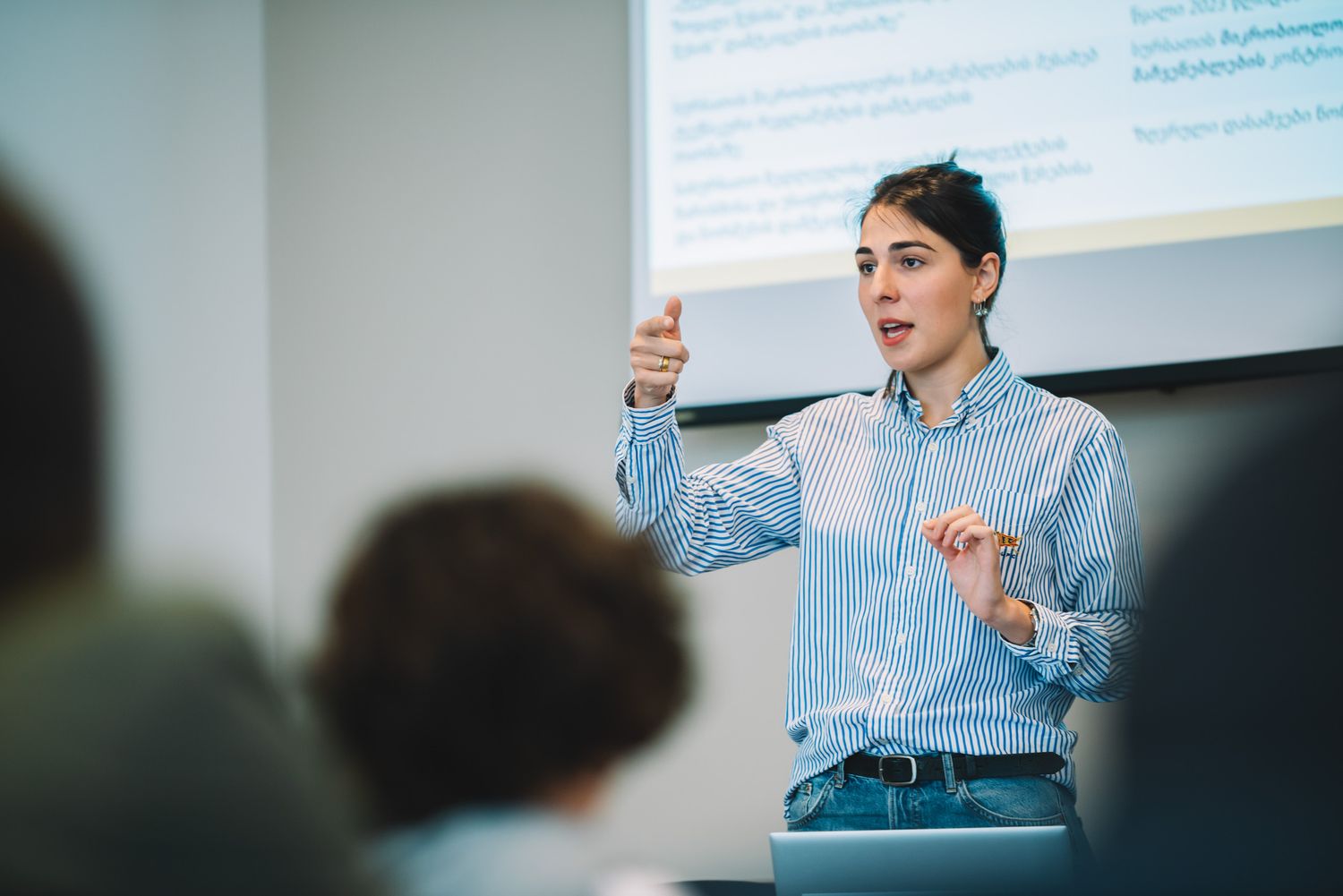 Female speaker presenting in front of a screen during an indoor training session.