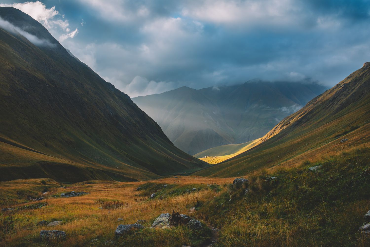 Lush green mountain valley under a dynamic blue sky with scattered clouds — panoramic view from the Caucasus.