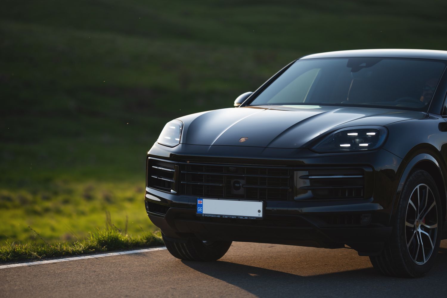 Side-angle shot of a sleek black SUV parked near grassy fields — moody lighting.