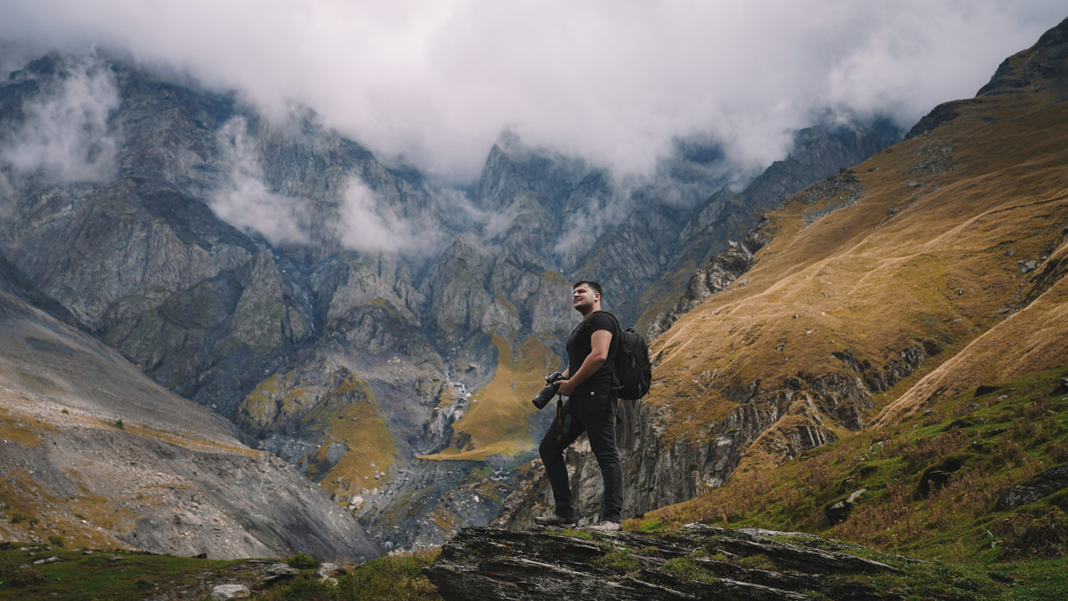 Man hiking through a dramatic mountain valley with moody skies—excellent for adventure, travel, or outdoor gear branding.