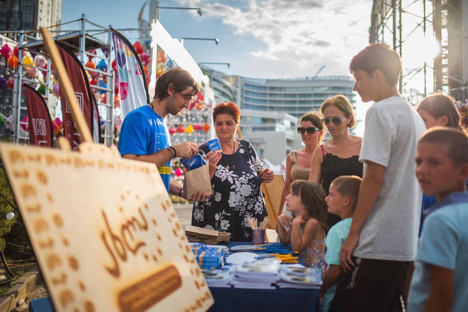 Festive open-air event with smiling people, crafts table, and cultural flags—ideal for travel, local culture, or volunteer projects.