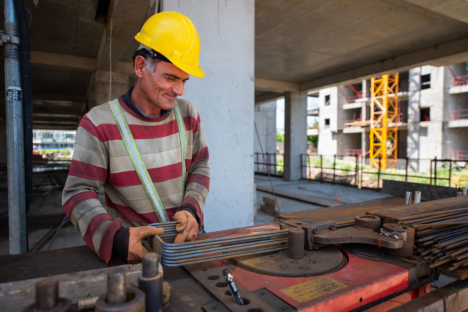Construction worker wearing a helmet and safety gear, operating rebar cutting tools on site.