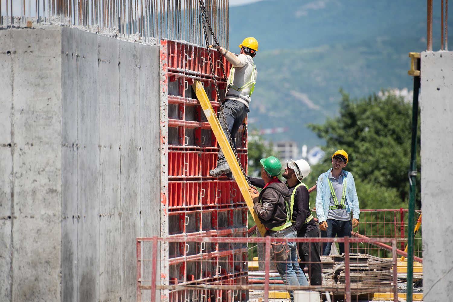 Team of construction workers preparing vertical concrete walls with red shuttering panels.
