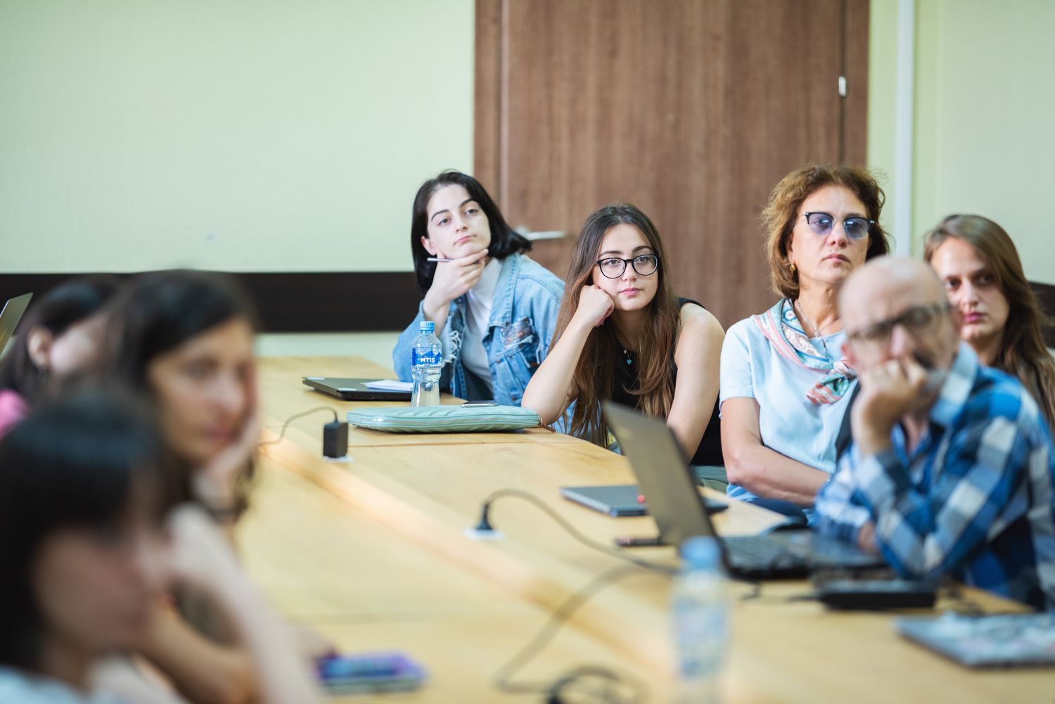 Attentive group of young women sitting around a conference table in a classroom setting.