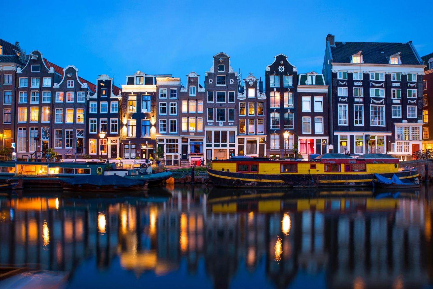 Canal houses of Amsterdam lit up at night — colorful architecture with water reflections.