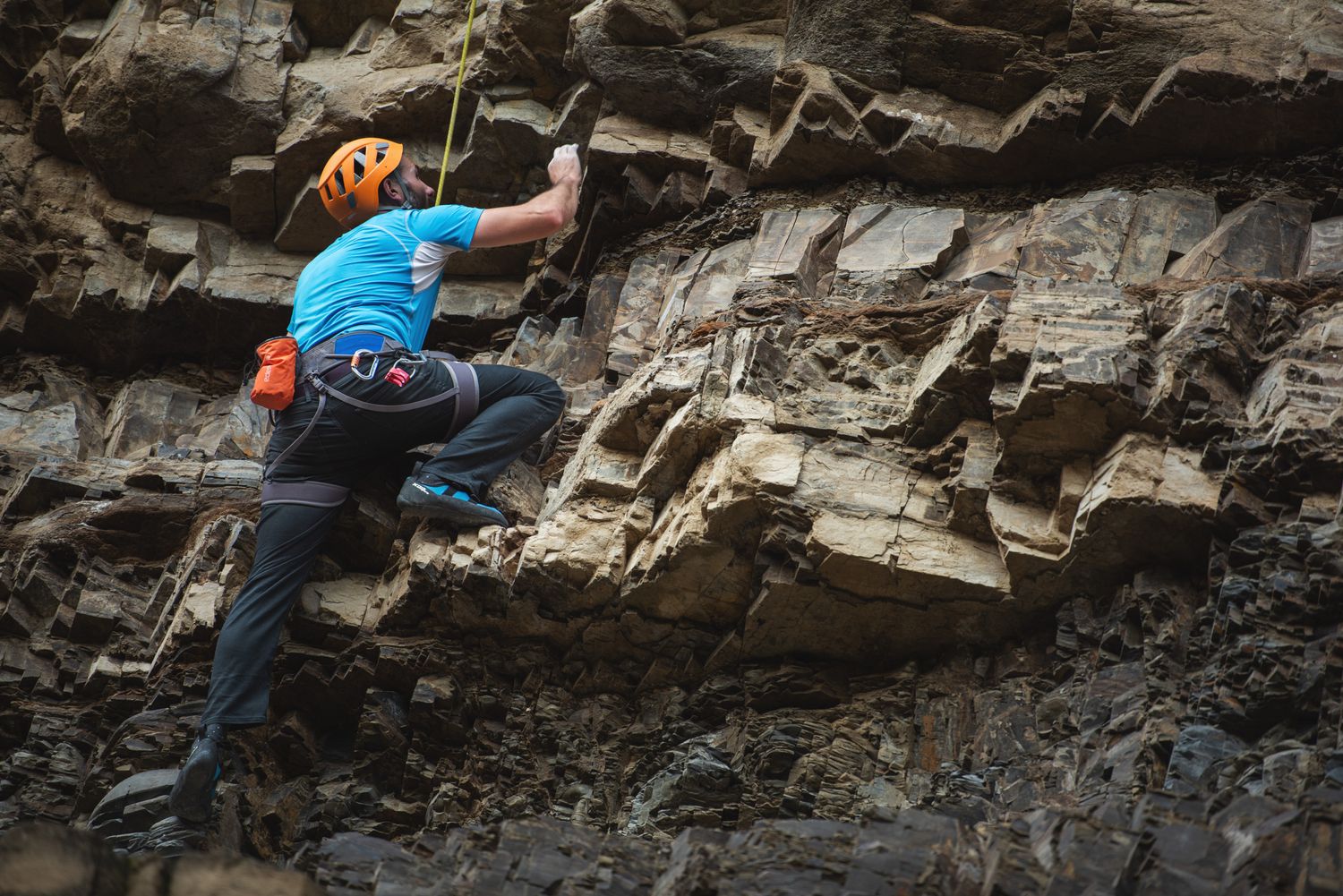 Man climbing a rock face with safety gear in an outdoor canyon environment.