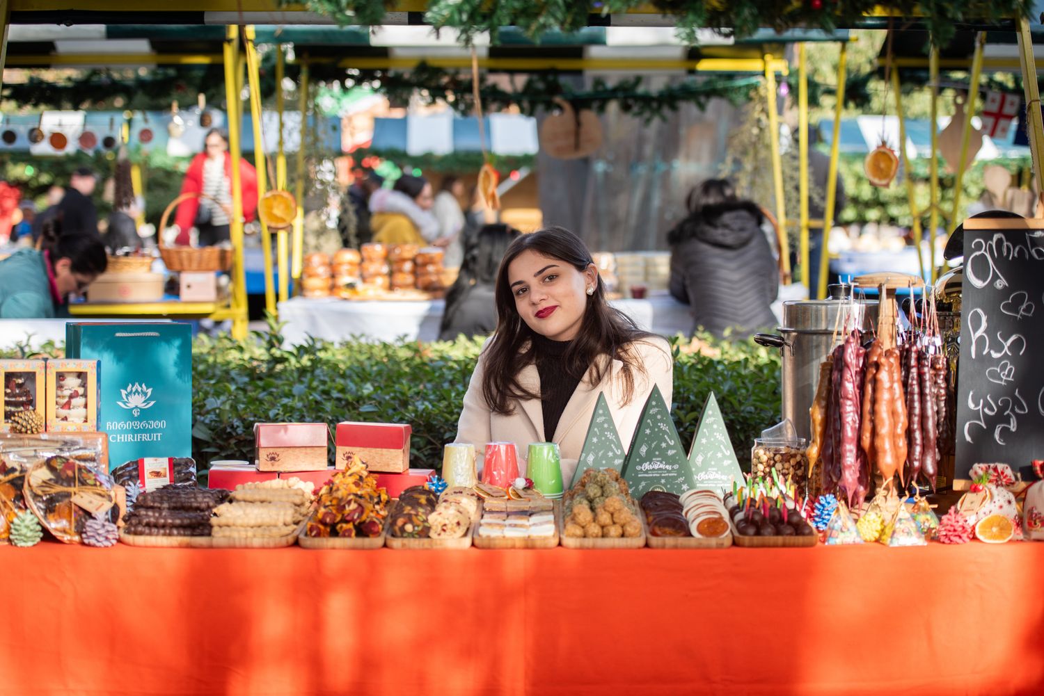 Two women showcasing handmade products and natural goods at a colorful market stall.