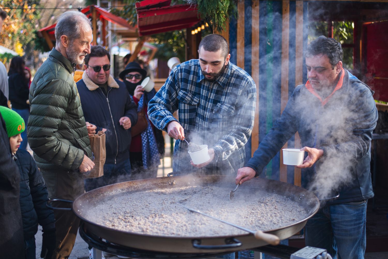 Chefs preparing food in a giant cauldron at a traditional street food event.