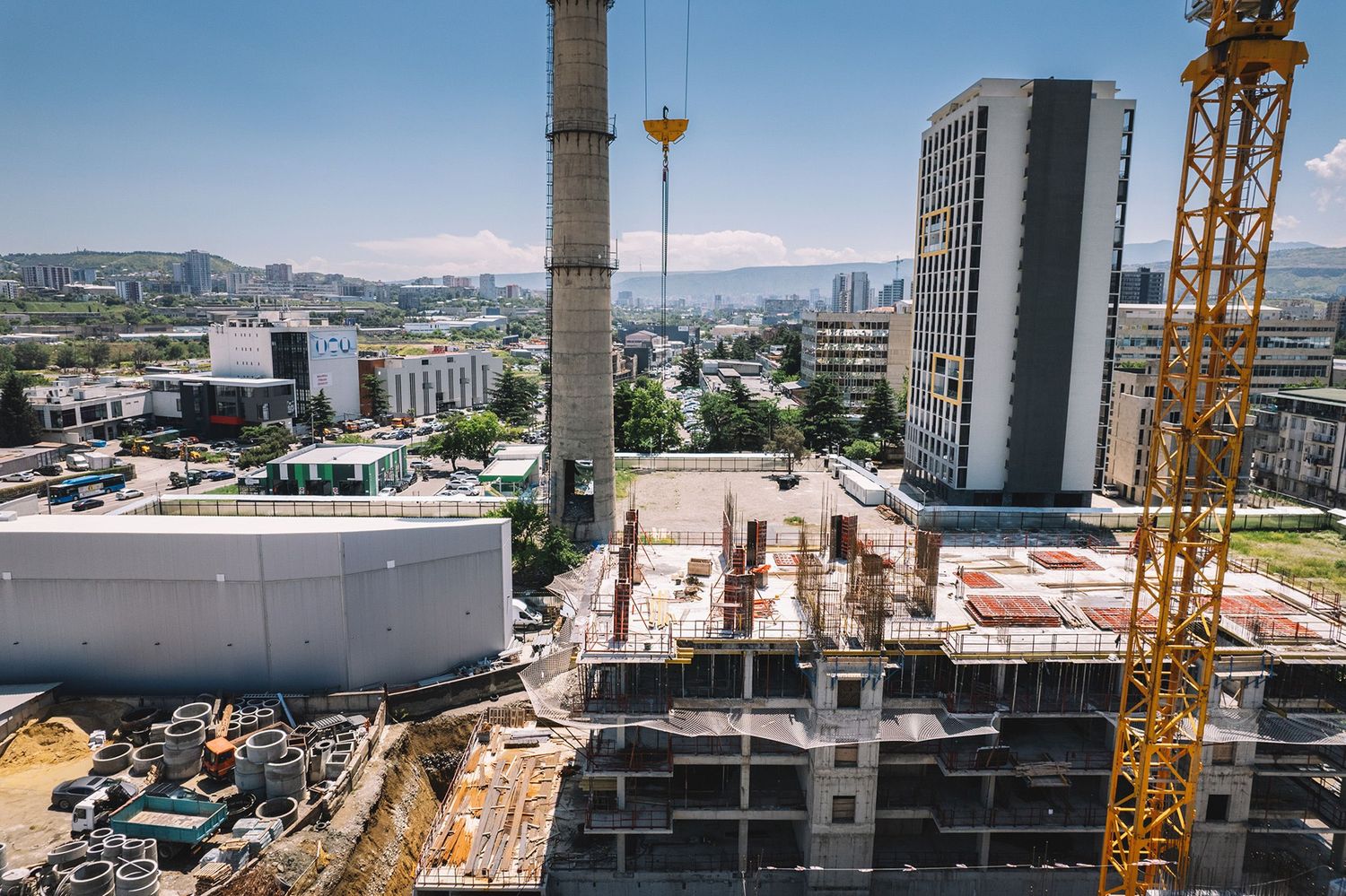 Aerial view of urban construction site surrounded by tall buildings and cranes in progress.