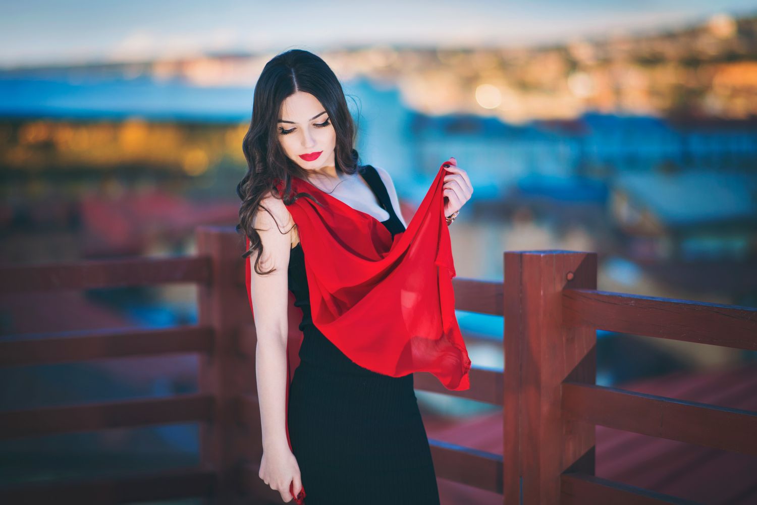 Smiling woman in red scarf posing near a railing with waterfront background — vibrant outdoor portrait.