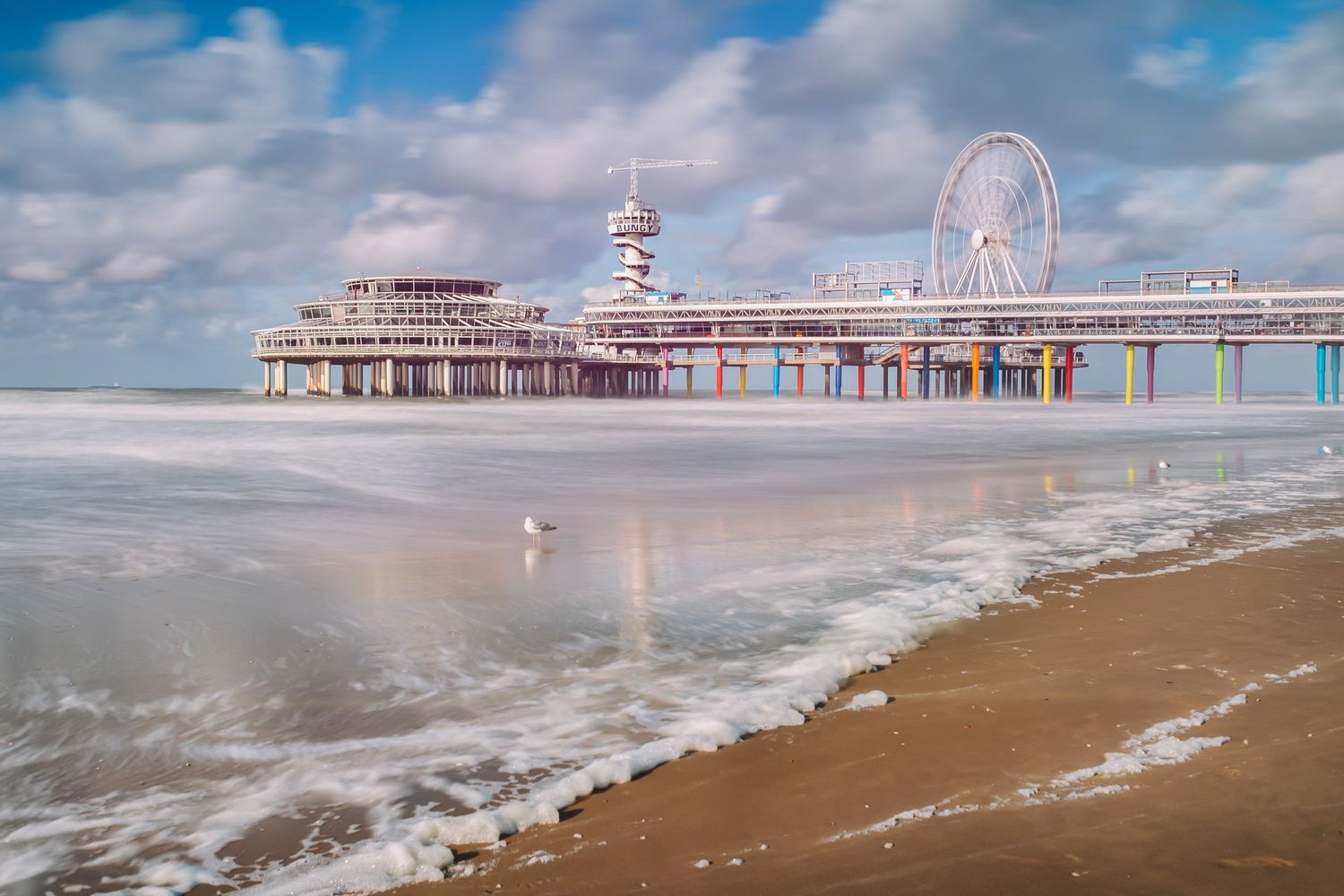 Bright coastal pier with a Ferris wheel on a sandy beach — vibrant seaside attraction.