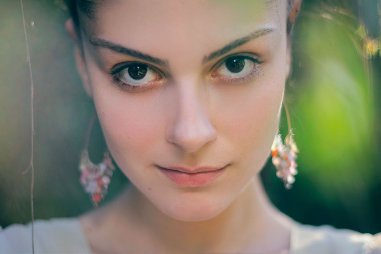 Close-up of a woman with expressive eyes and earrings — soft-focus beauty shot.