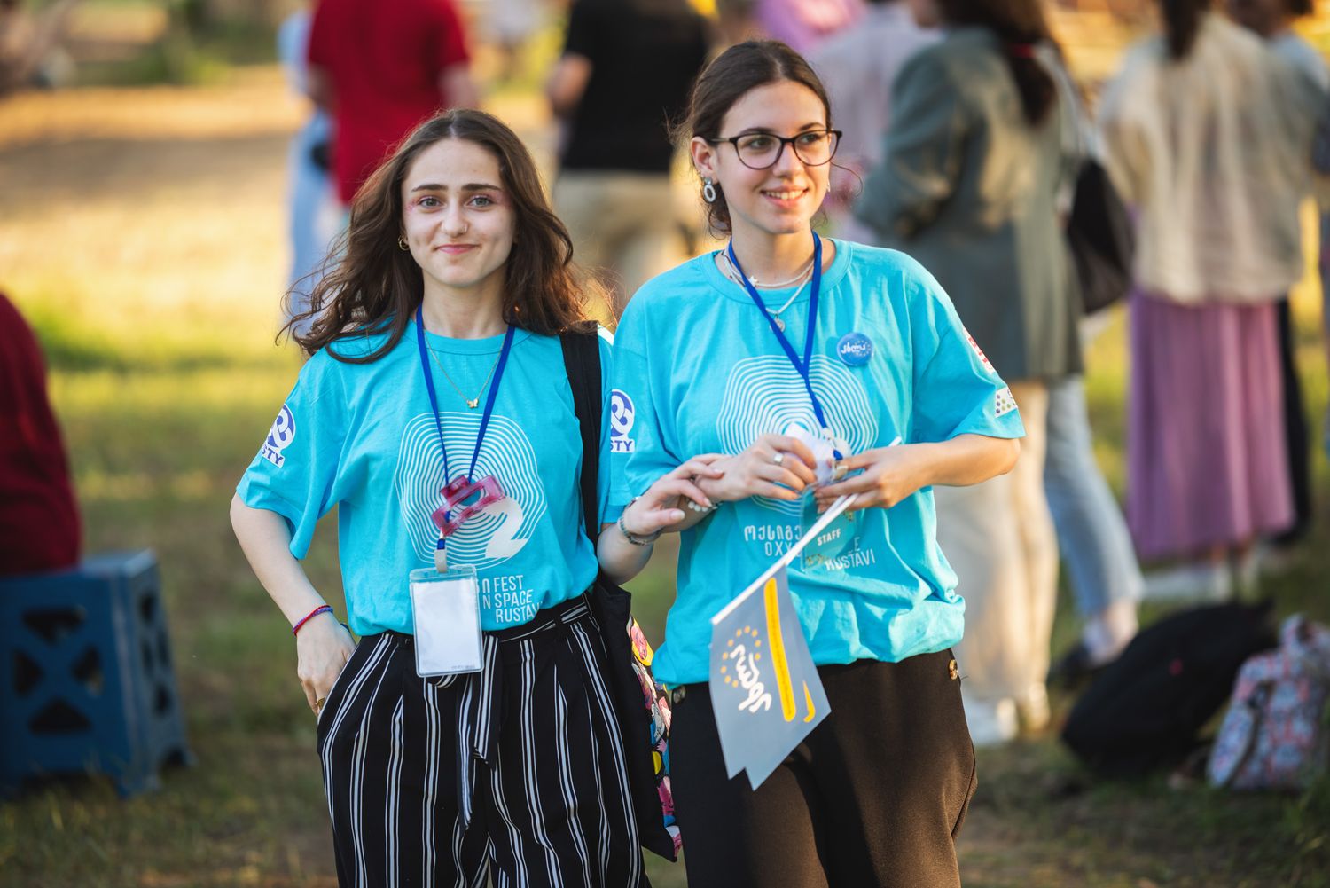 Two young women wearing campaign T-shirts and holding materials at an outdoor event.