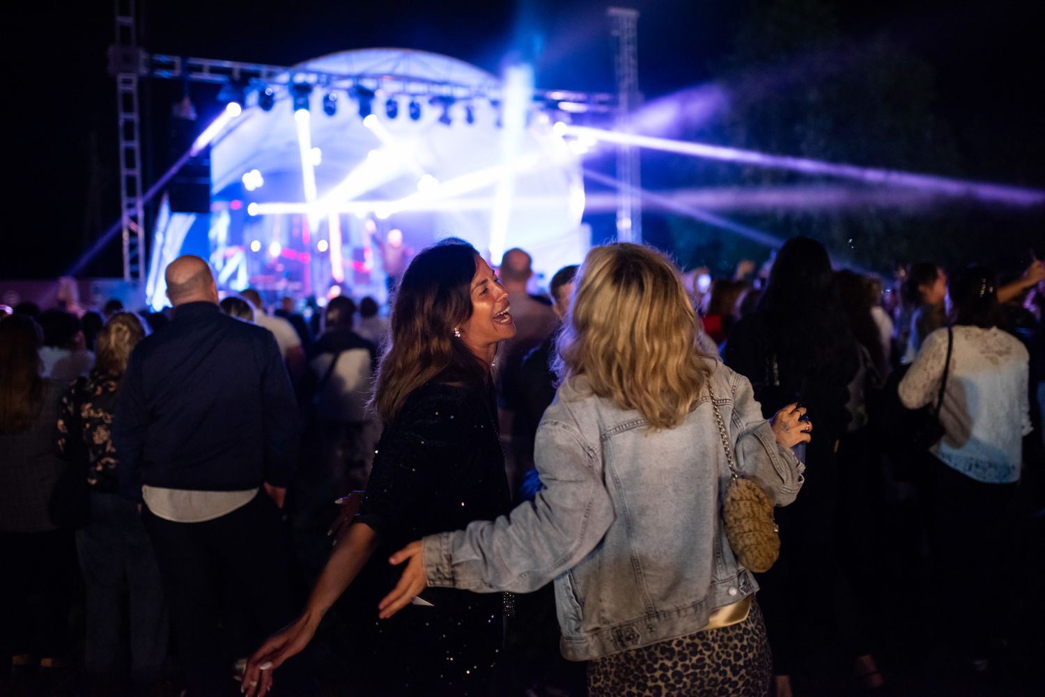 Group of friends dancing under bright stage lights during a lively nighttime outdoor concert.