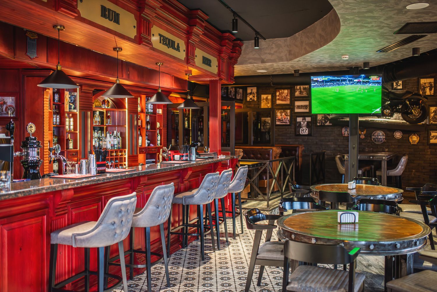 Lively sports bar with bold red counter, bar stools, and wall-mounted television, styled with a mix of industrial and retro design.