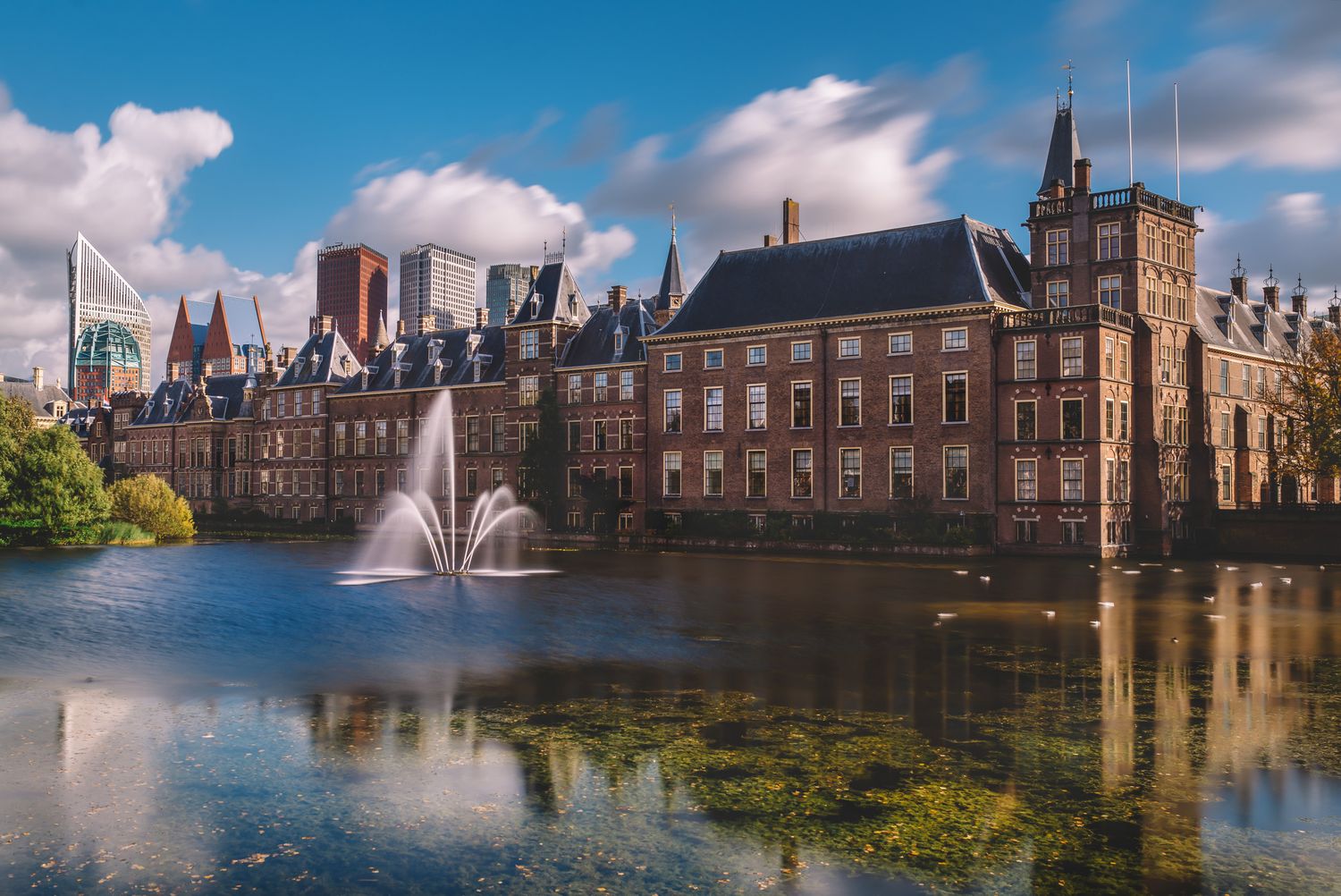 The Binnenhof government complex in The Hague, reflected in a central pond on a clear day.