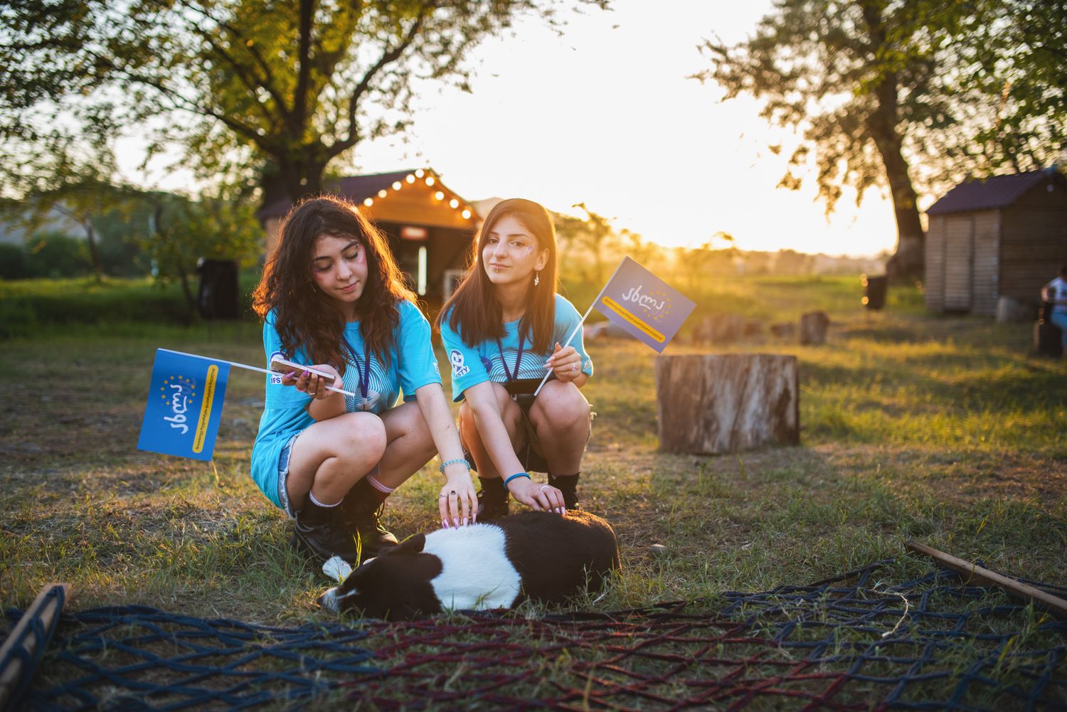 Group of girls sitting on grass with gift bags, enjoying a relaxed moment at sunset.