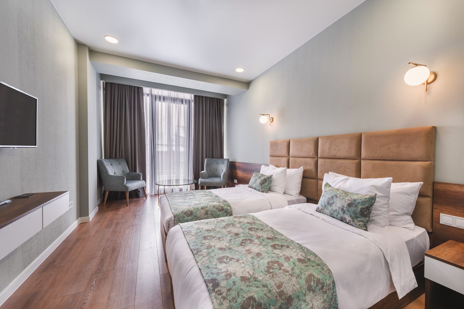 Contemporary hotel room with wooden flooring, double bed, and soft lighting, creating a warm and relaxing atmosphere.