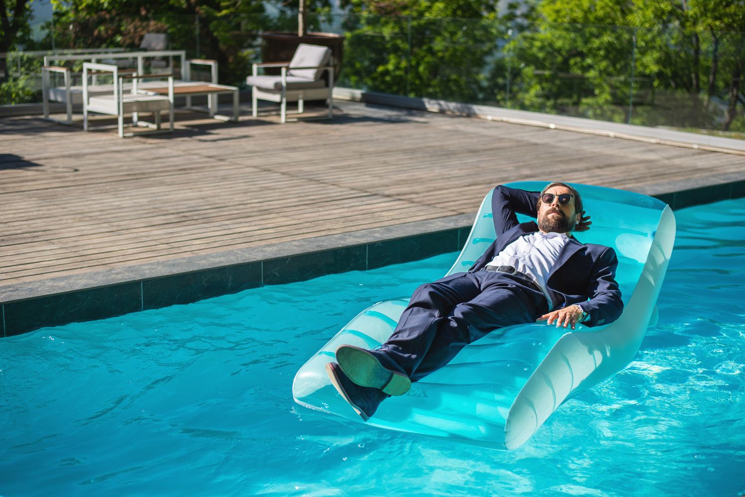 Man in business attire floating on an inflatable raft in swimming pool — humorous work-life contrast.