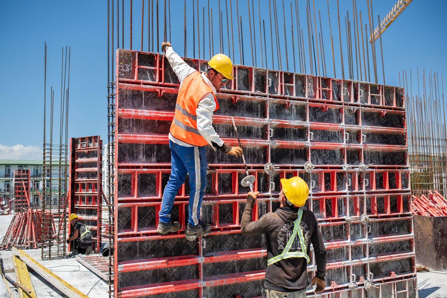 Crew of builders securing and aligning red steel shuttering panels for vertical wall construction.